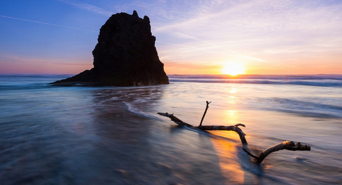 standing rock offshore in calm sea with driftwood