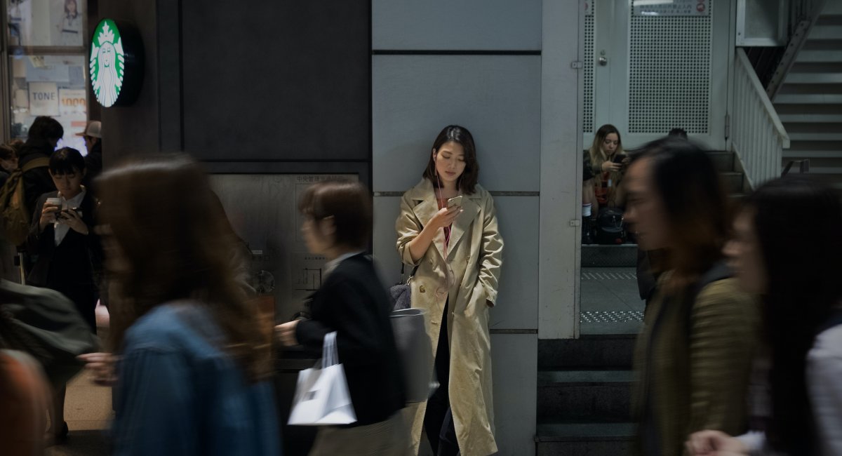 A woman leaning against a wall, scrolling on her phone in the city centre