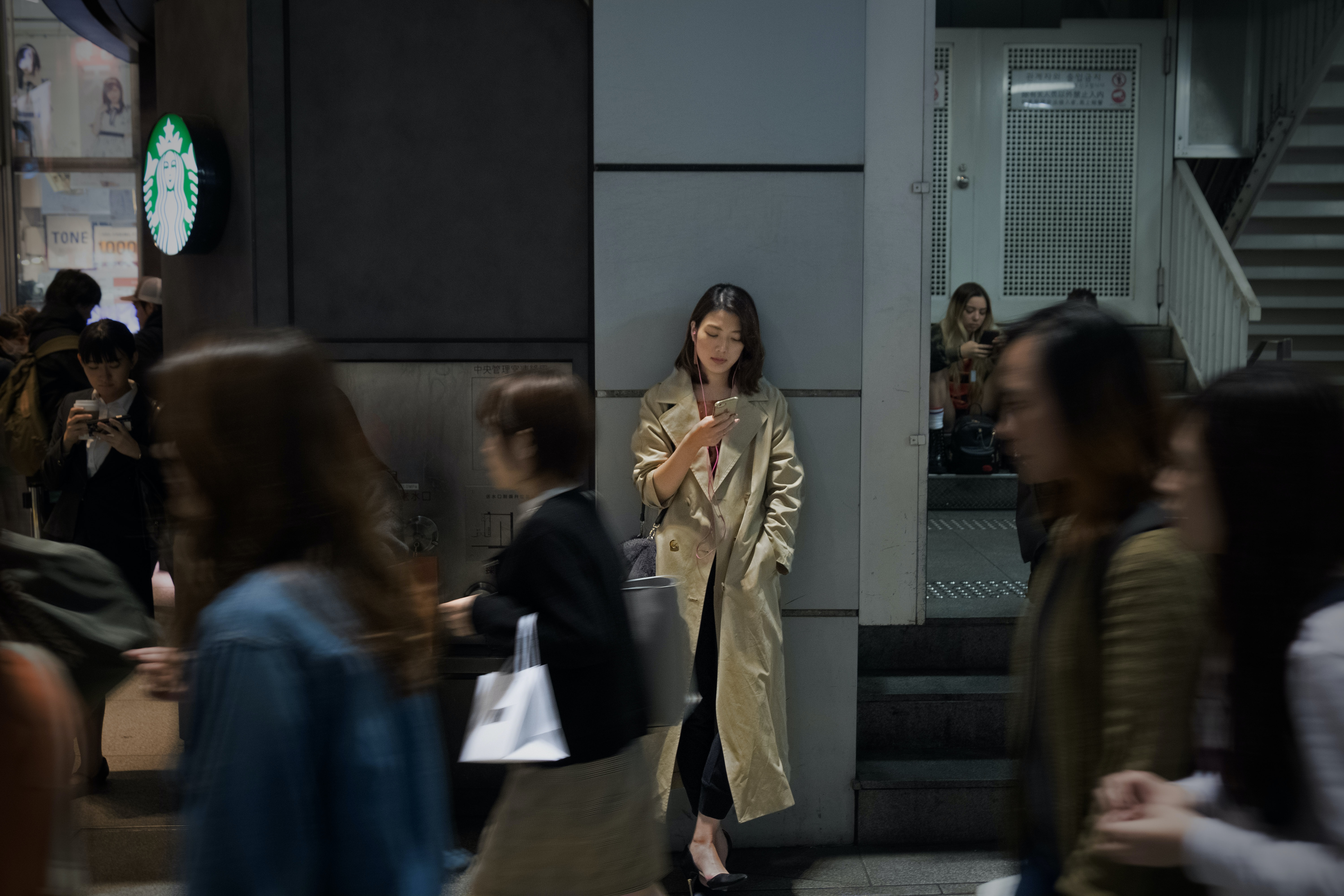 A woman leaning against a wall, scrolling on her phone in the city centre