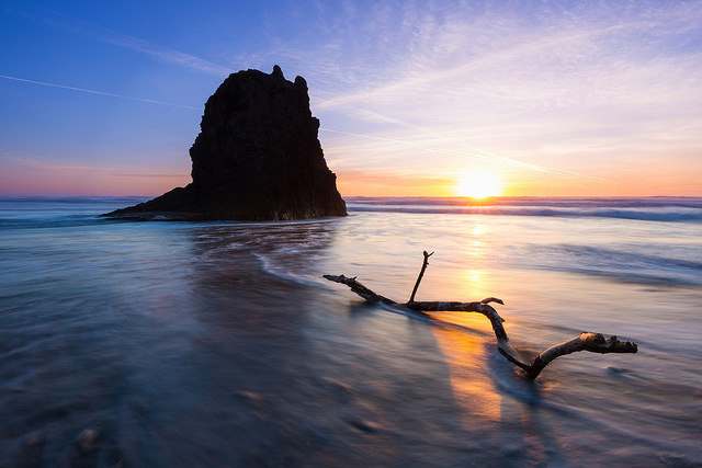 standing rock offshore in calm sea with driftwood