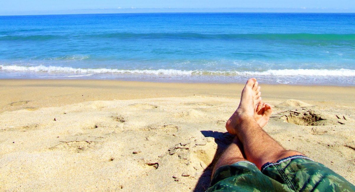 Man's legs on a beach by a calm ocean.