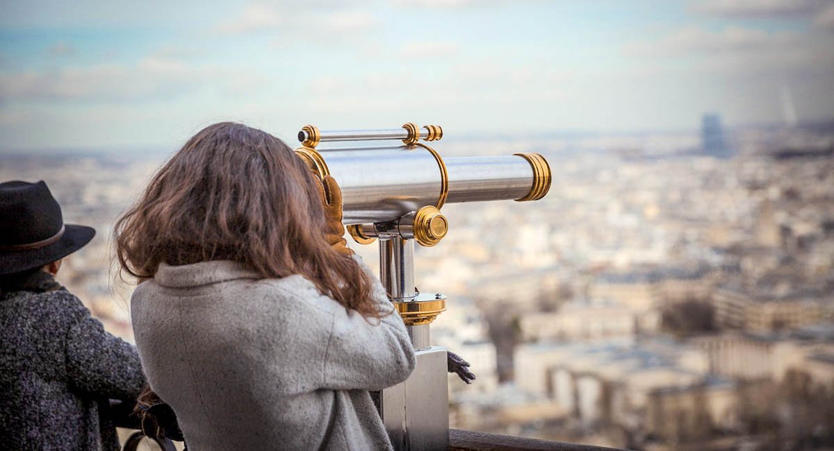 Person using telescope on skyscraper looking over city