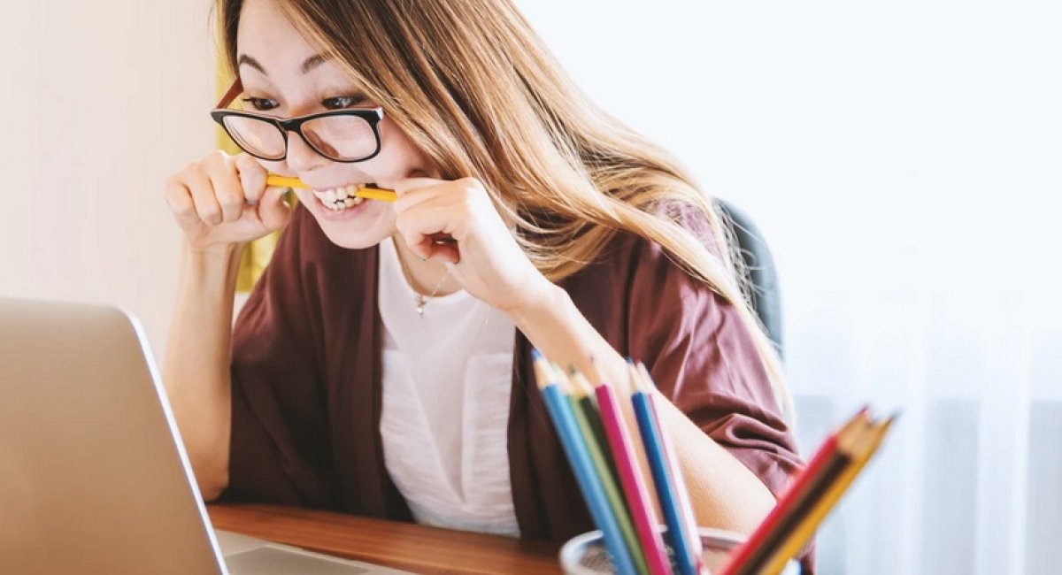 Woman at computer with pencil between her teeth looking upset